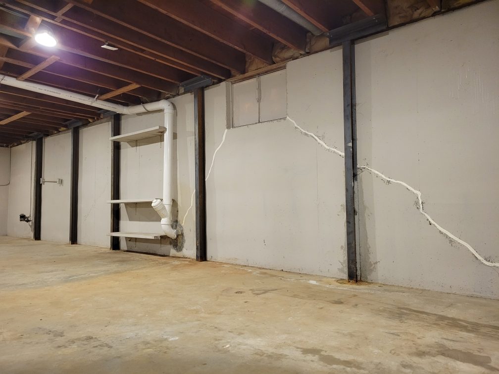 Long crack running down a poured concrete basement wall between steel wall restraints